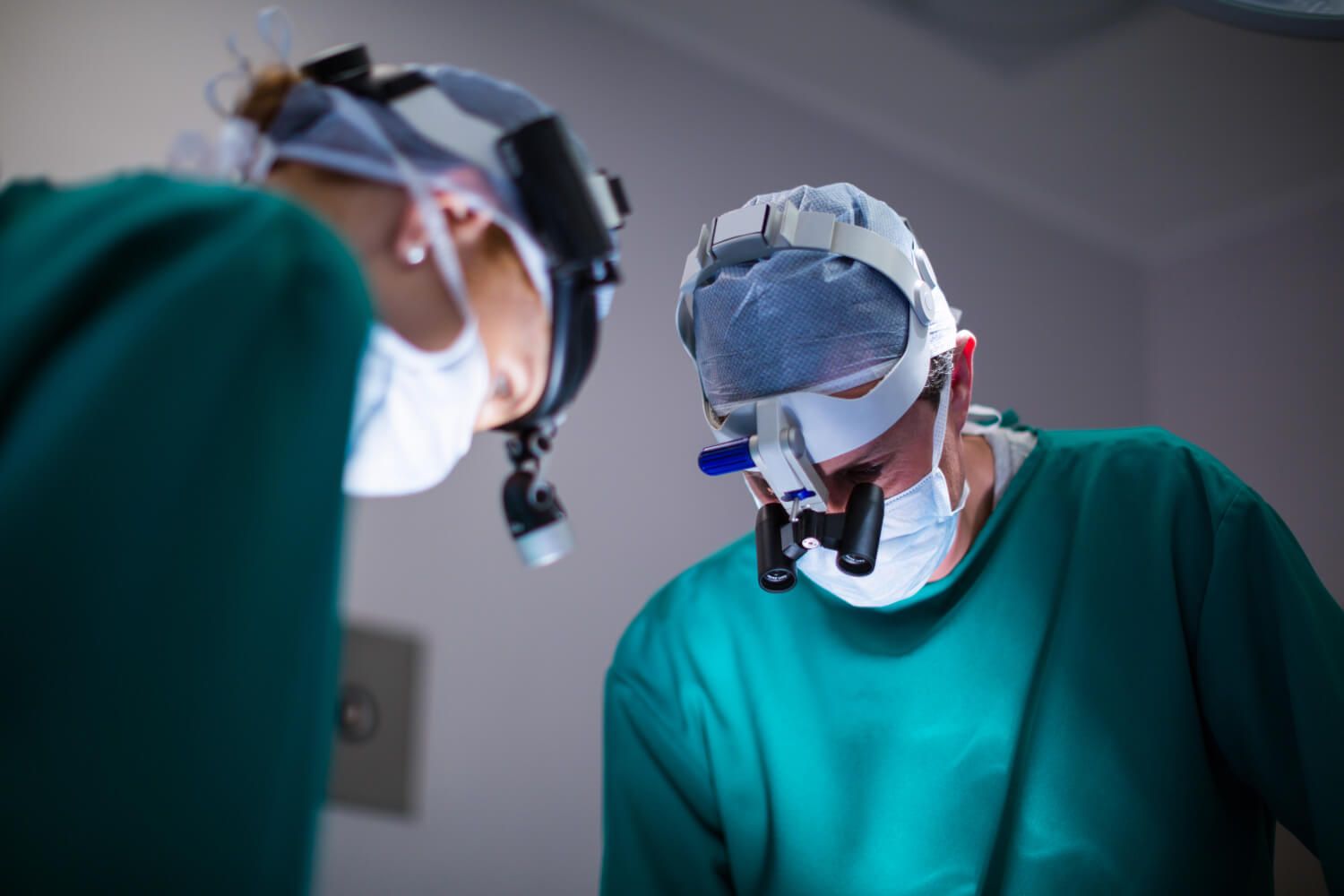 Хирург смотрит на операционное поле через бинокулярную хирургическую лупу